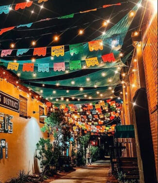 bishop arts district at night bishop arts district at night an alley way with Papel Picado flapping in the wind interspersed with string lights